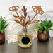 A glass reed diffuser bottle with a silver cap and a decorative wooden flower stem reed, styled on a dark tabletop with two potted succulents in the background.