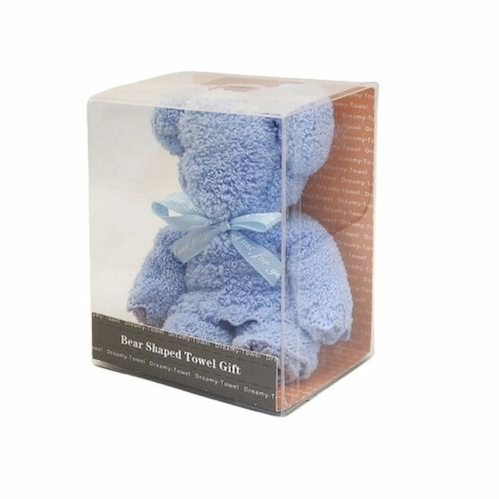 A bear-shaped towel gift in a clear plastic cube package, featuring a light blue plush towel bear with a matching blue ribbon bow and a dark label at the bottom.