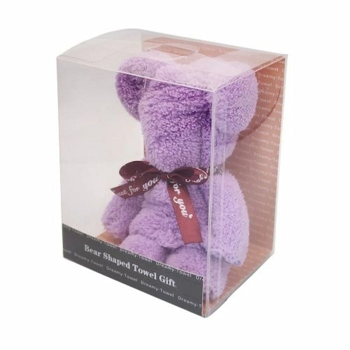 A lavender purple teddy bear shaped towel gift inside a clear plastic display box with a dark base label. The bear has a dark brown ribbon tied around its neck with 'be you' printed on it.