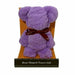 A purple plush teddy bear-shaped towel gift sitting in an orange patterned chair, tied with a dark red bow that says 'you are', with a black label at the bottom reading 'Bear Shaped Towel Gift'.