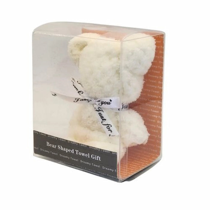A bear-shaped cream-colored towel gift inside a clear plastic box with an orange patterned backing and a black label at the bottom. The towel features a white ribbon tied around the neck with black script text.