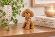 A small plush dog figurine made of gold-toned beads sits on a wooden shelf, styled with a potted plant, books, and a lit candle in a warm indoor setting.