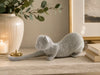A sculptural cat figurine covered in small silver rhinestones, posed stretching on a light stone mantel with a cream vase, candle, and framed art in the background.