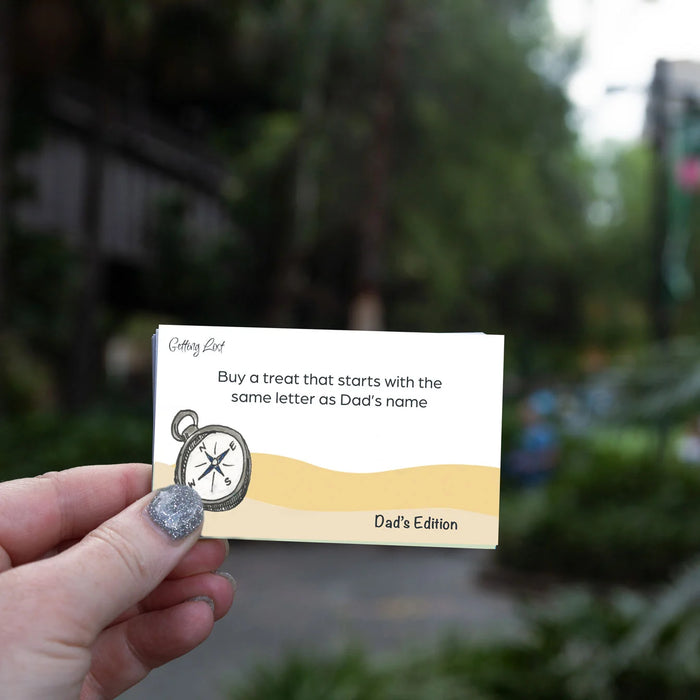 Hand holding a card with text and a compass graphic, blurred outdoor background