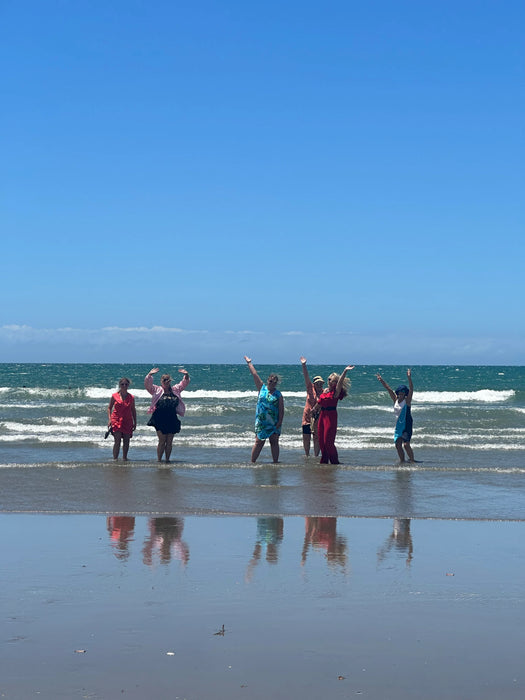 Group of people on a beach with arms raised, enjoying the view.