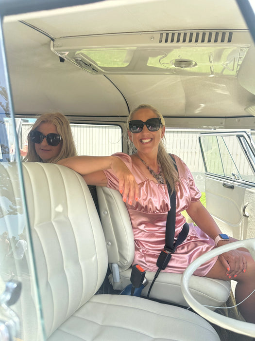 Two women sitting inside a vintage vehicle with a white interior.
