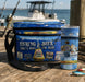 Fishing-themed cooler and cup with beer and fish graphics on a dock by the water.