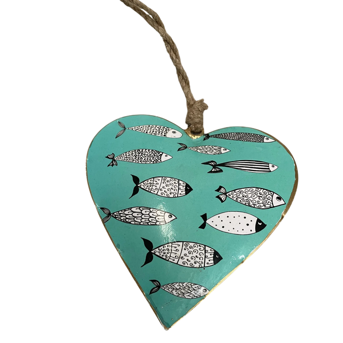 A heart-shaped metal hanging ornament with a turquoise background, decorated with black and white patterned fish, and suspended by a natural twine string.