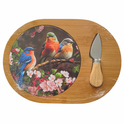 An oval bamboo serving board with a printed circular inset showing three colorful birds perched among pink flowers. A small knife with a light wood handle and silver blade rests on the right side of the board, all photographed on a plain white background.