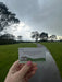 Hand holding a card with instructions on a road with grass and trees in the background