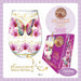 A clear stemless wine glass decorated with pink orchids, a blue and purple butterfly, gold crescent moons, and gold glitter details, shown next to a matching purple gift box labeled '24K Gold Cocktail Garnish'. The image includes promotional text and decorative borders.