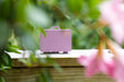 Pink carrying case with 'Ganging Art' branding on a wooden surface with greenery and pink flowers in the background.