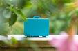 Blue suitcase with 'Gaming Lab' branding on a blurred natural background