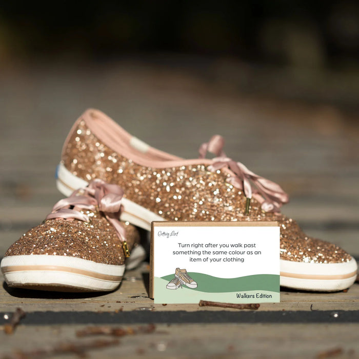 Gold glittery shoes with pink laces on a wooden surface, accompanied by a card.