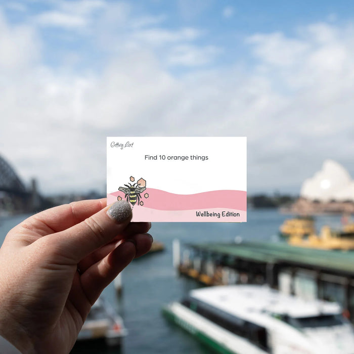 Hand holding a card with text and illustration against a blurred waterfront background