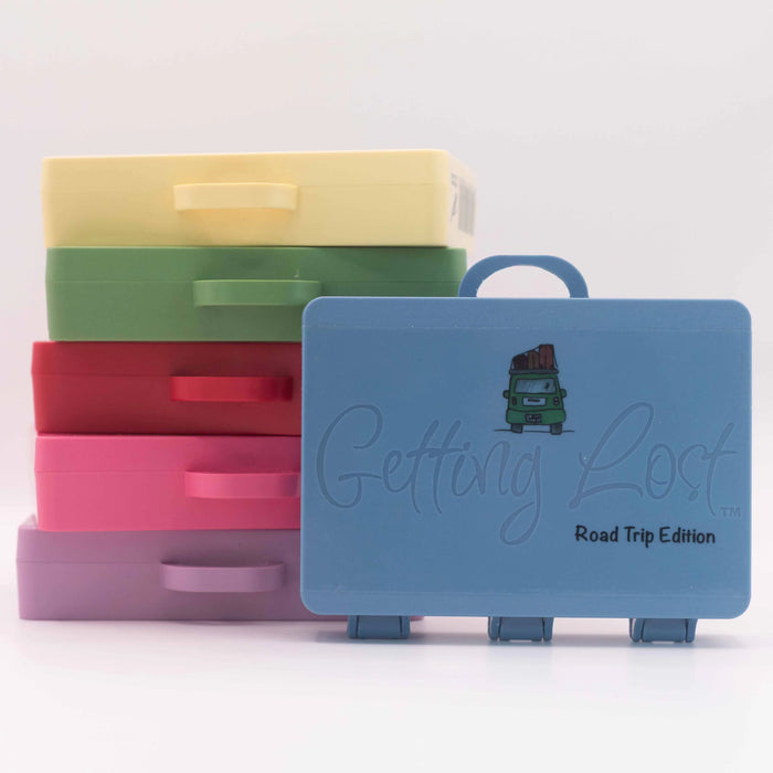 Stack of colorful plastic suitcases with a blue one labeled 'Getting Lost Road Trip Edition' on a light gray background.