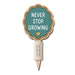 A wooden garden stake with a scalloped sign that reads 'NEVER STOP GROWING' in white text on a teal background, with a small gold heart and layered wood borders, on a white background.