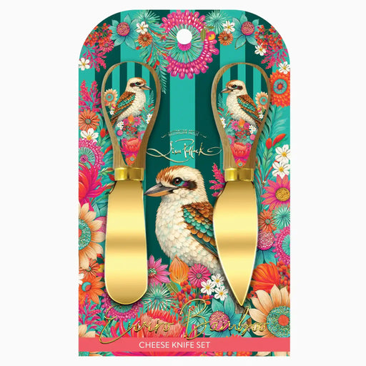 A decorative cheese knife set in its retail packaging, featuring two gold-colored cheese knives with handles printed with a colorful kookaboo and floral design on a teal and pink striped background.
