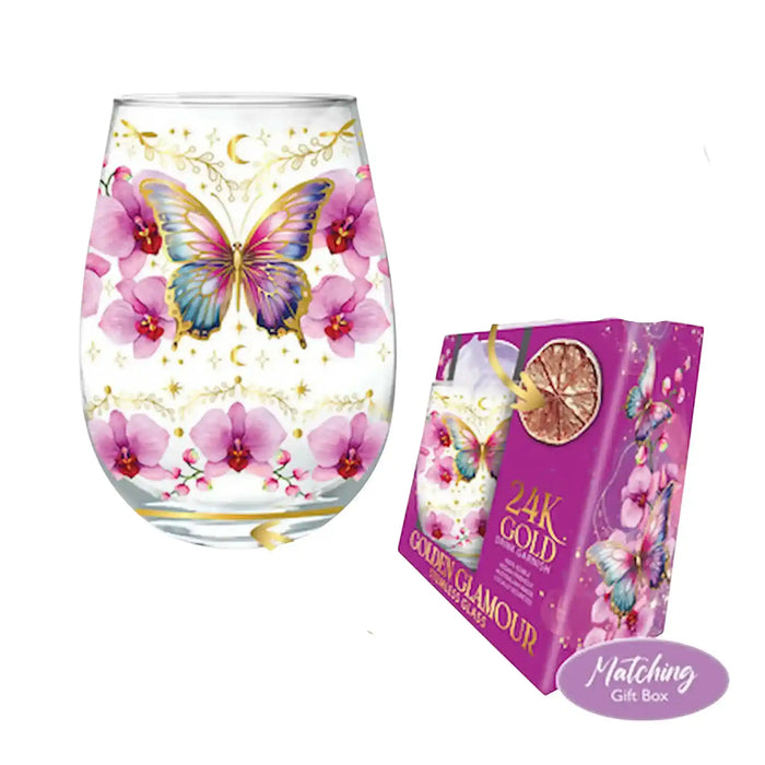A clear stemless wine glass decorated with pink orchids, a blue and purple butterfly, gold crescent moon and star motifs, shown next to its purple gift box. A purple badge in the corner reads 'Matching Gift Box'.
