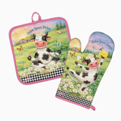 A matching kitchen set featuring a square pot holder and an oven mitt with a colorful cartoon cow illustration on a grassy field, butterflies, flowers, and the text 'Calm Your Farm.' The set has pink trim, a black-and-white gingham band, and a white background.