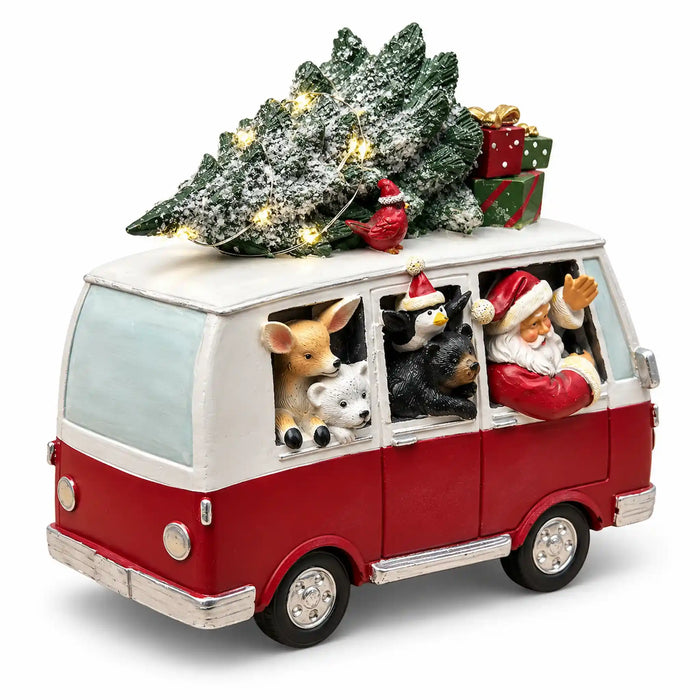 A festive Christmas decoration of a red and white vintage VW bus carrying a snow-dusted Christmas tree on its roof, with Santa, a deer, a cat, a dog, and a bird waving out the windows, set against a plain white background.