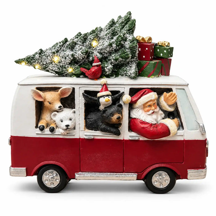 A festive red and white Christmas van figurine with Santa Claus, a deer, a polar bear, a penguin, and a small bird peeking out of the windows. A snow-dusted Christmas tree with warm lights and wrapped gifts sits on the roof, all on a clean white background.