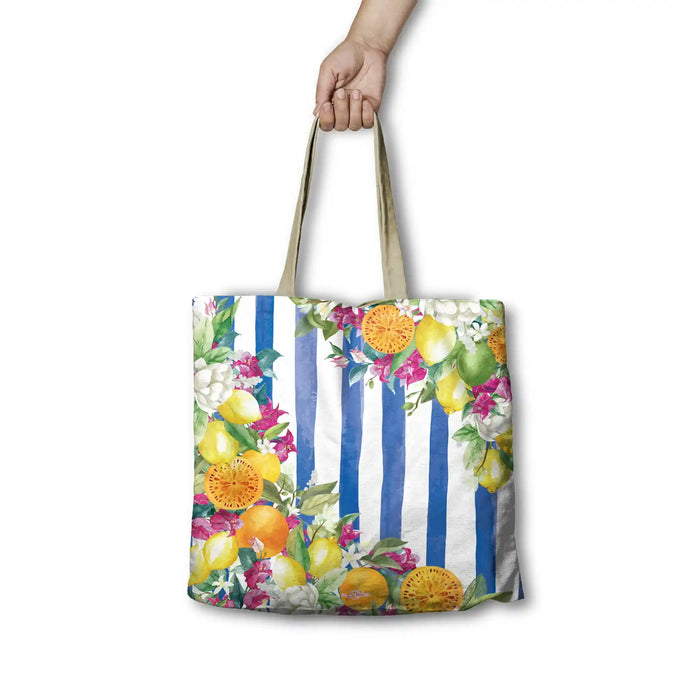 A tote bag with a blue and white striped background and a colorful watercolor floral and fruit print, held by a hand against a white background.