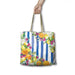 A tote bag with a blue and white striped background and a colorful watercolor floral and fruit print, held by a hand against a white background.