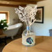 Decorative diffuser with floral design on a wooden table in a room with a bathtub and plant.