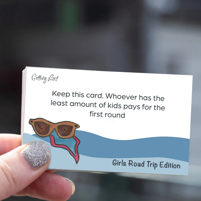 A hand with glittery silver nail polish holds a small printed card that reads, 'Keep this card. Whoever has the least amount of kids pays for the first round' with an illustration of sunglasses above blue wavy lines.