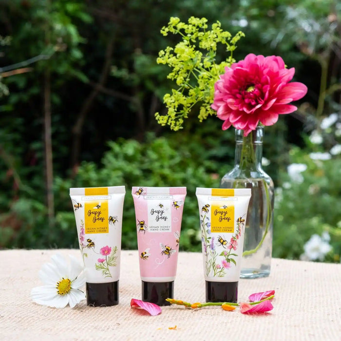 Three tubes of Honey Glow skincare cream and clay mask are arranged on a burlap table outdoors with a green garden background, styled with flowers.