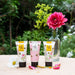 Three tubes of Honey Glow skincare cream and clay mask are arranged on a burlap table outdoors with a green garden background, styled with flowers.