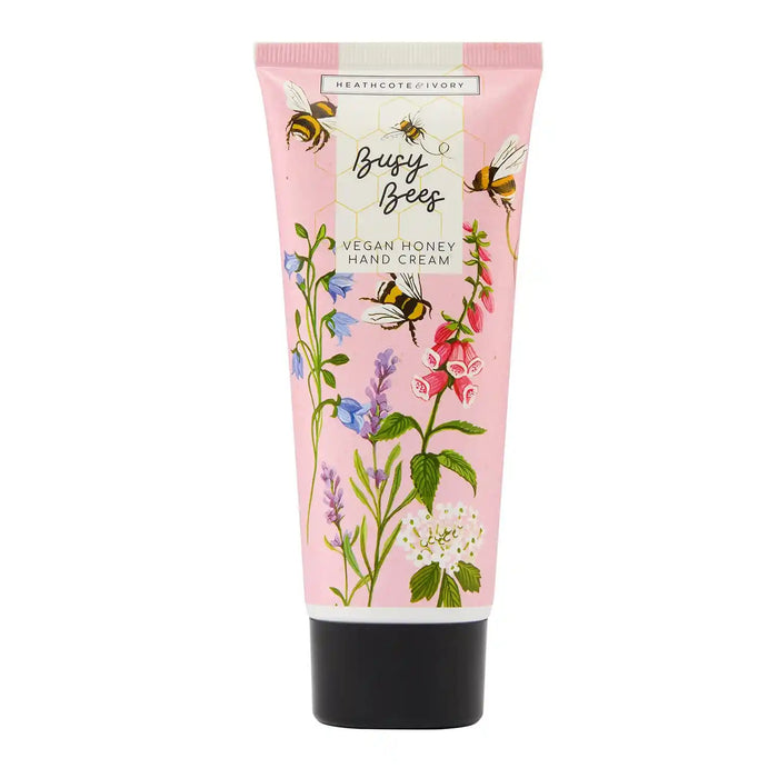 A pink tube of Heathcote & Ivory Busy Bees Vegan Honey Hand Cream, decorated with illustrations of bees and wildflowers, on a white background.