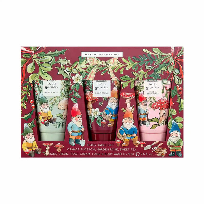 Heathcote & Ivory 'In the Garden' body care set in a decorative gift box, containing three tubes: orange blossom hand cream, garden rose foot cream, and sweet pea hand & body wash, decorated with gnome illustrations and holly motifs.