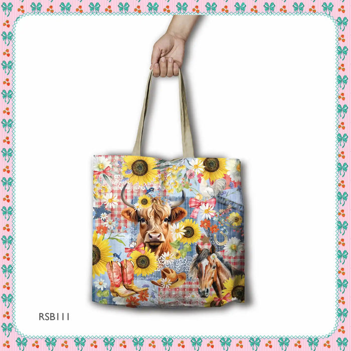 A tote bag with a colorful western-themed print featuring a cow, sunflowers, boots, and a horse, held by a hand against a white background with a decorative border.