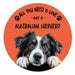 A circular coaster featuring a black and white Australian Shepherd dog peeking up against a bright orange background, with the text 'ALL YOU NEED IS LOVE - AND A AUSTRALIAN SHEPHERD' in black lettering and small paw prints.