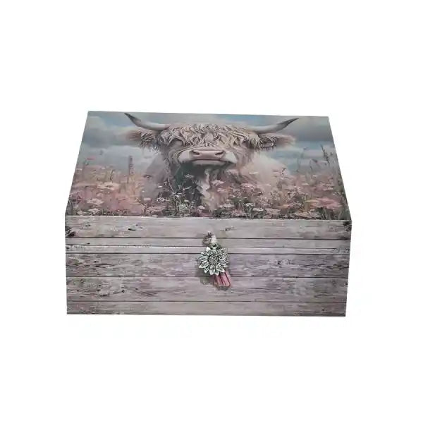 A rectangular decorative box with a rustic wood-grain finish, featuring a printed highland cow and wildflower design on the lid and front, with a small tassel ornament on the clasp, shown against a plain white background.