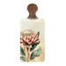 A rectangular wooden cutting board with a rounded top handle, featuring a vintage-style illustration of a pink and cream protea flower with green leaves on a light beige background.