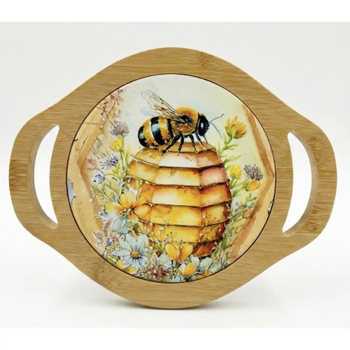 A round bamboo serving platter with two side handles and a central printed illustration of a honeybee on a beehive surrounded by yellow and white flowers, shown on a white background.