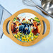 A round bamboo serving board with two side handles and a colorful printed illustration of four cows in a flower field, shown on a light blue surface with a whisk and metal bowl nearby.