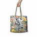 A tote bag with a printed illustration of a koala and its joey surrounded by colorful flowers, held by a hand against a plain white background.