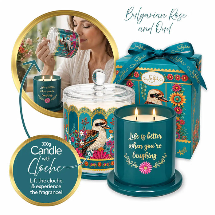 A decorative teal scented candle set with a glass jar candle, a lit candle in a teal holder, a matching gift box with a blue ribbon, and a circular inset showing a woman holding a matching candle. The packaging and labels feature kookaboo and floral artwork, with text reading 'Bulgarian Rose and Oud' and 'Life is better when you're laughing.