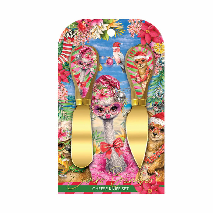 A Christmas-themed cheese knife set in its original packaging. The set features two gold-colored cheese knives with pink and green striped handles, decorated with festive illustrations of a cat in a pink bonnet, a dog in a Santa hat, and a Christmas tree.