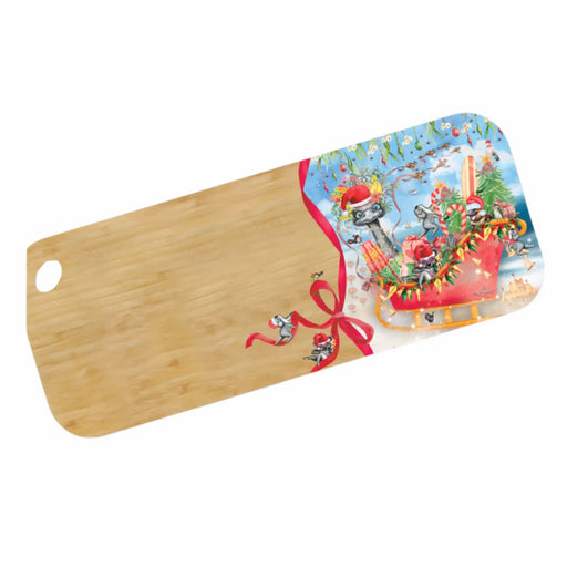 A rectangular wooden cutting board with rounded corners and a hole in one corner, featuring a printed Christmas scene on the right side with Santa, sleigh, tree, ornaments, and a red ribbon bow.