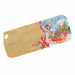 A rectangular wooden cutting board with rounded corners and a hole in one corner, featuring a printed Christmas scene on the right side with Santa, sleigh, tree, ornaments, and a red ribbon bow.