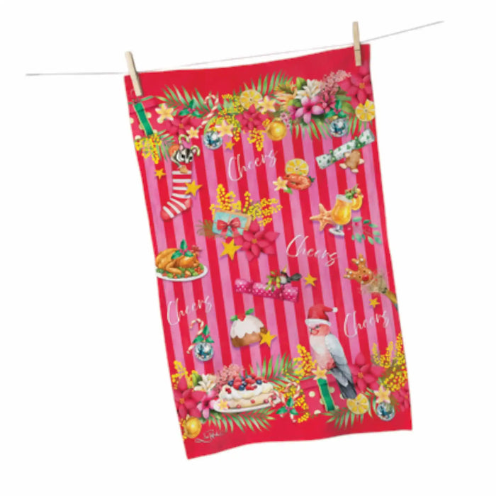 A festive Christmas tea towel with a red and pink striped background, decorated with stockings, ornaments, a nutcracker, cakes, and the word 'Cheers' repeated across the front. The towel is shown hanging from a clothesline with wooden clothespins against a plain white background.