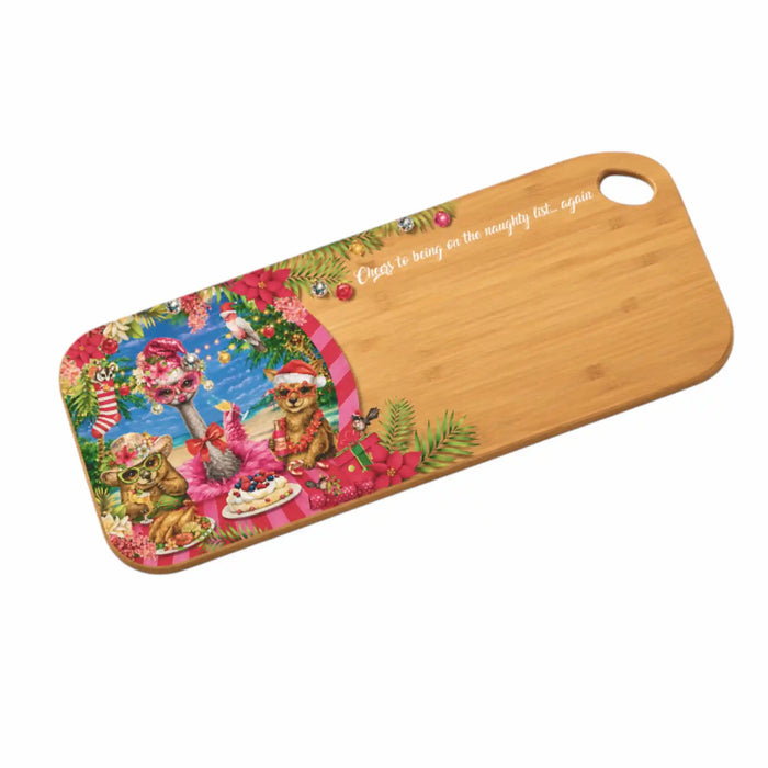 A rectangular bamboo cutting board with rounded corners and a built-in handle, featuring a colorful Christmas-themed illustration on one end and the white cursive text 'Cuts to bring on the naughty list.