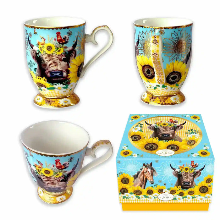 Three views of a decorative ceramic mug with a matching gift box, featuring a cow, sunflowers, and birds on a light blue background with gold trim.