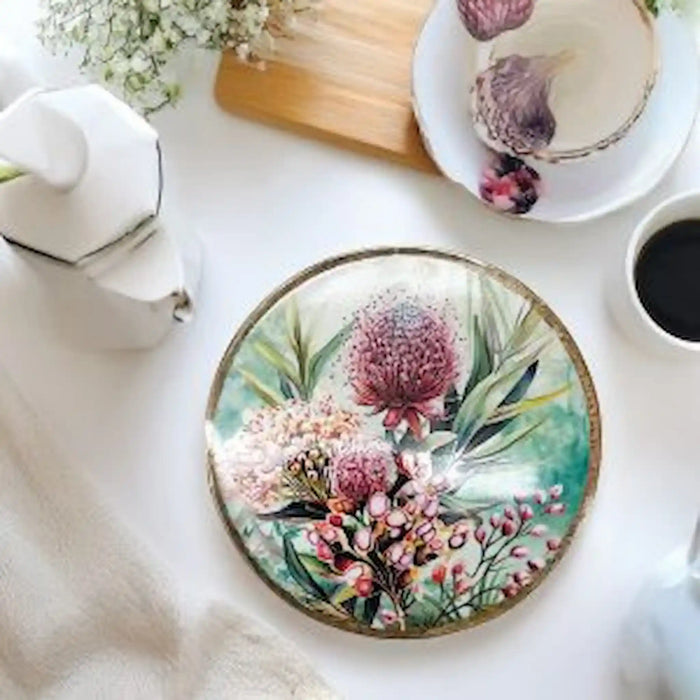 Midnight Australiana ceramic trivet with pink native flowers, styled on a dining table beside tea and coffee.