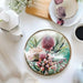 Midnight Australiana ceramic trivet with pink native flowers, styled on a dining table beside tea and coffee.